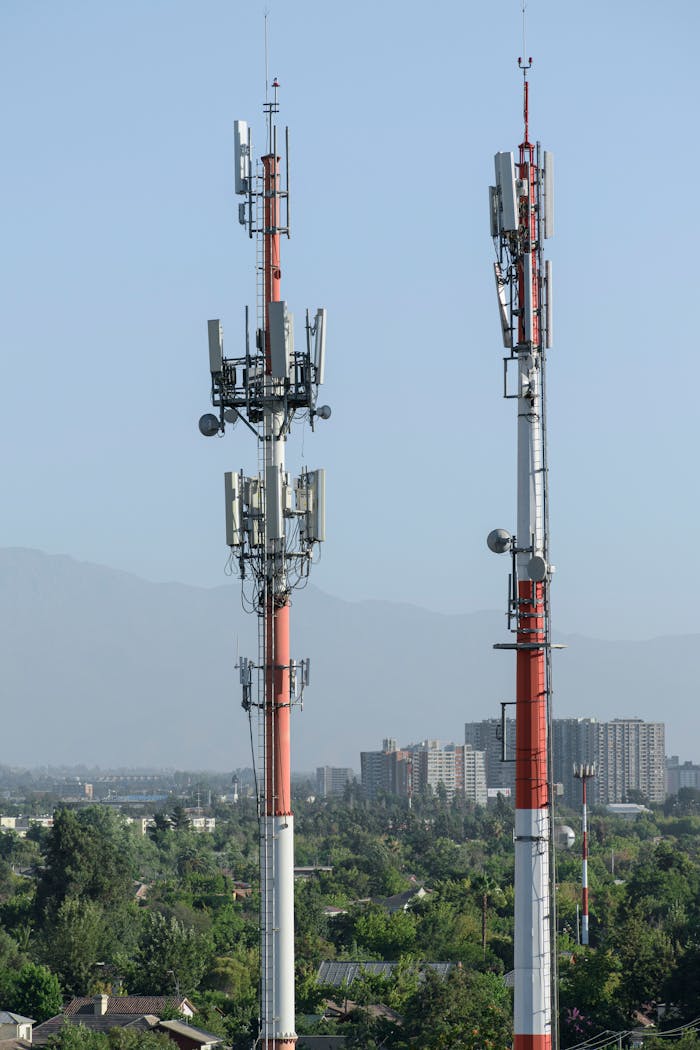 Two telecom towers overlooking a cityscape with distant mountains.