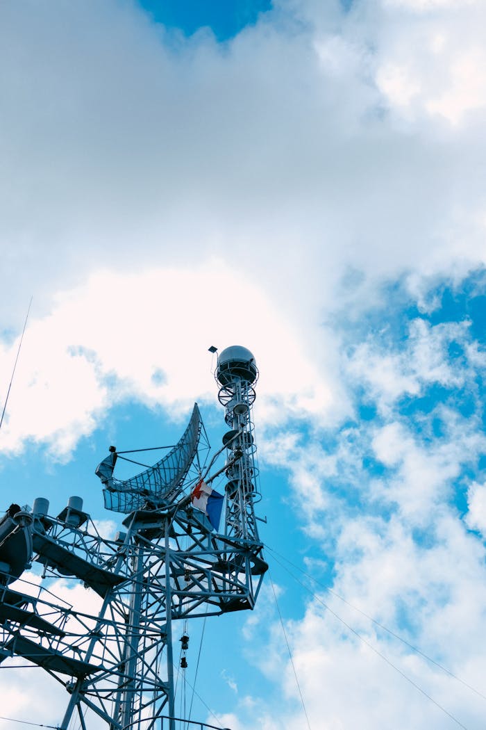 A steel television tower with antennas against a vibrant blue sky featuring scattered clouds.